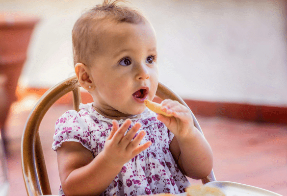 Bébé qui découvre un aliment coloré avec ses doigts, à table, sous le regard bienveillant d’un parent.