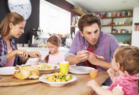 Parent et jeune enfant à table, souriants, mangeant ensemble dans une ambiance calme et lumineuse.