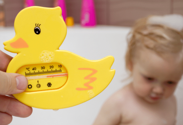 Parent vérifiant la température de l’eau du bain de bébé avec un thermomètre de bain (35–37 °C).