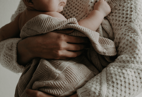 Maman berçant son bébé dans les bras, illustrant le contact et la réassurance avant le sommeil.