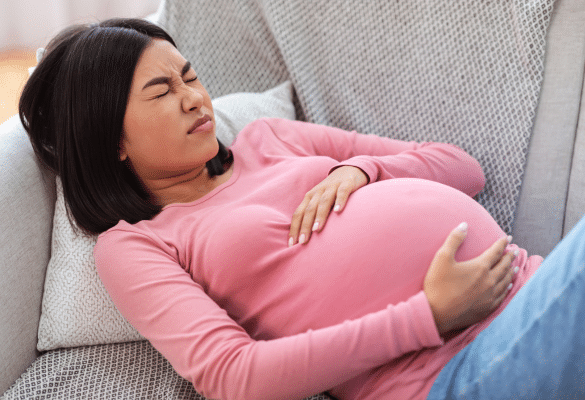Femme enceinte allongée sur un canapé, main sur le ventre, exprimant un inconfort digestif