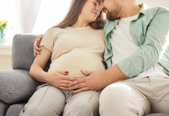 Couple de futurs parents assis, mains posées ensemble sur le ventre de la maman enceinte pour sentir les mouvements du bébé.