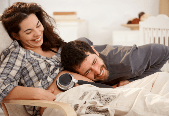 Couple de futurs parents allongés, main posée sur le ventre de la maman enceinte pour ressentir bébé bouger.
