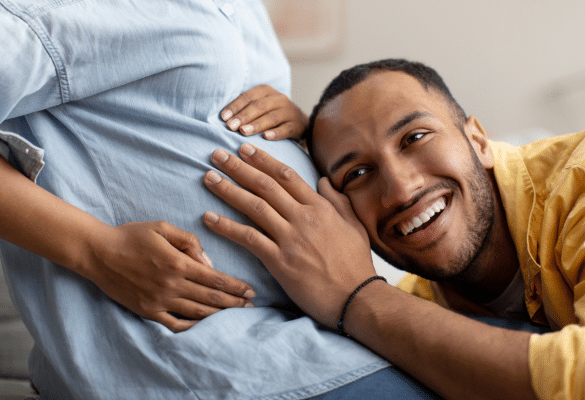 Futur papa posant sa tête et son oreille sur le ventre arrondi de la maman enceinte, moment complice avec bébé.