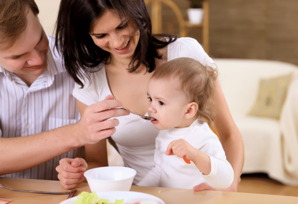 Bébé mangeant à table avec ses parents, entouré de petits plats adaptés à son âge