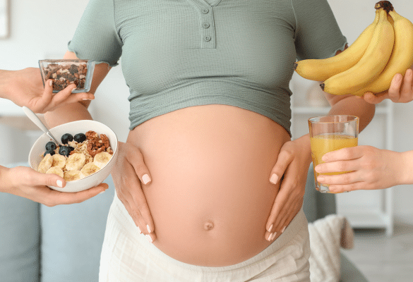 future maman enceinte avec un bol de céréales et des fruits. Envie de sucré ou de salé ? Ces envies font partie des croyances amusantes pour deviner le sexe.