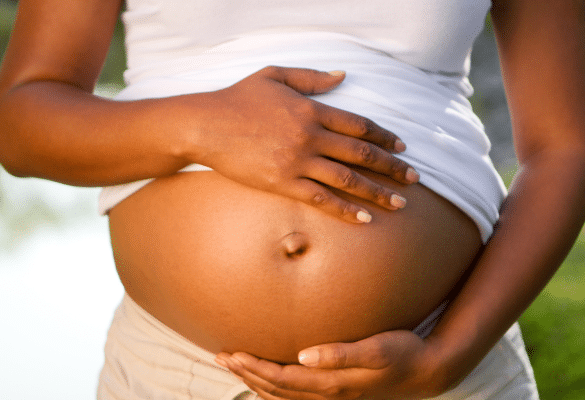 gros plan sur un ventre de femme enceinte avec des mains protectrices. La forme du ventre est souvent citée parmi les croyances populaires sur le sexe du bébé.