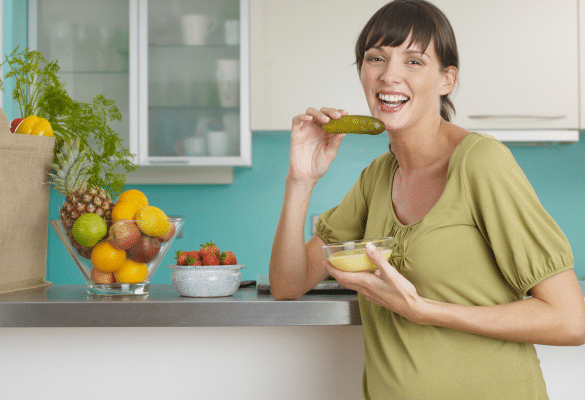 Femme enceinte dans une cuisine avec des aliments frais, illustrant les envies alimentaires pendant la grossesse