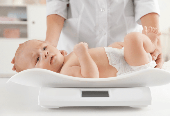 Bébé pesé sur une balance médicale par un professionnel de santé lors d’une consultation.