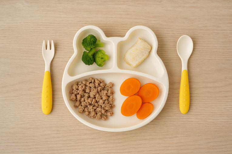 Assiette compartimentée contenant de petites portions de viande, poisson et légumes adaptées à l’âge de bébé