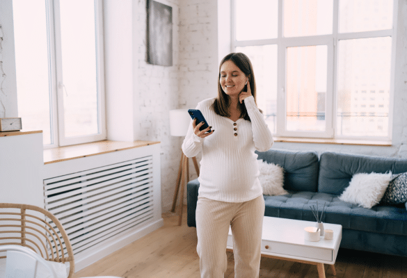 Jeune femme enceinte tenant une tablette en visio avec un message “Bébé en route” affiché à l’écran