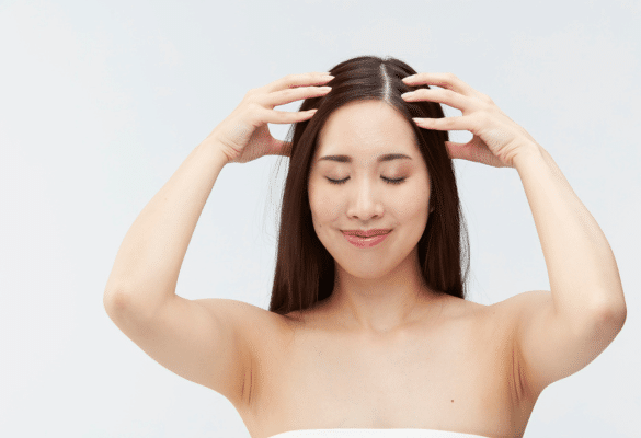 Jeune mère se massant le cuir chevelu chez elle, symbole de soin et de détente pendant le post-partum