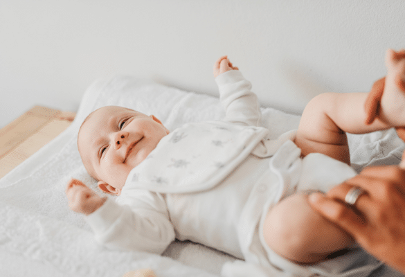Bébé allongé sur le dos, bras relevés, expression éveillée et joyeuse.