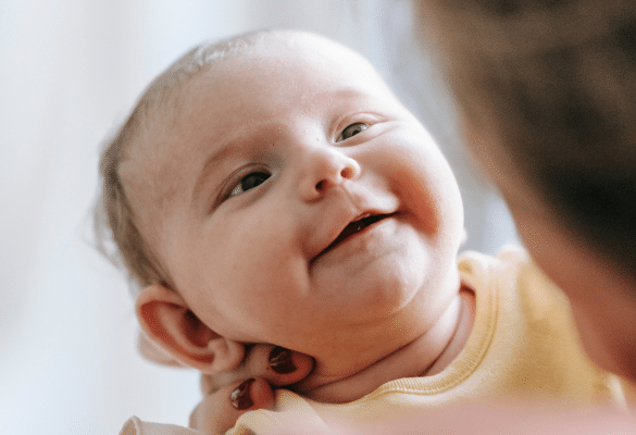Bébé de quelques semaines qui sourit doucement, regard lumineux.