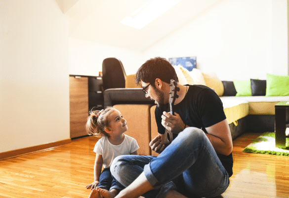Parent assis au sol face à son bébé, dans un salon lumineux, partageant un moment de jeu et de vocalises. Le bébé observe, sourit et émet des sons en réponse.