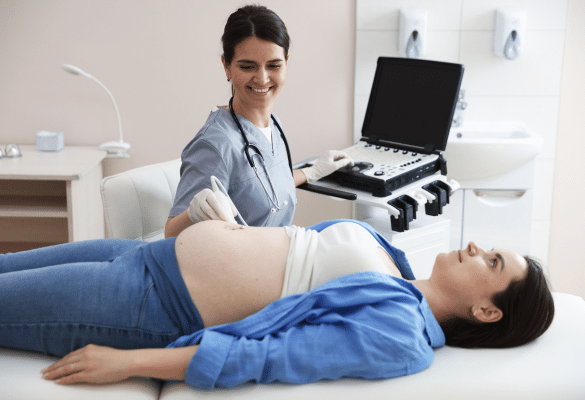 Sage-femme effectuant une échographie de grossesse gémellaire avec une future maman allongée et souriante.