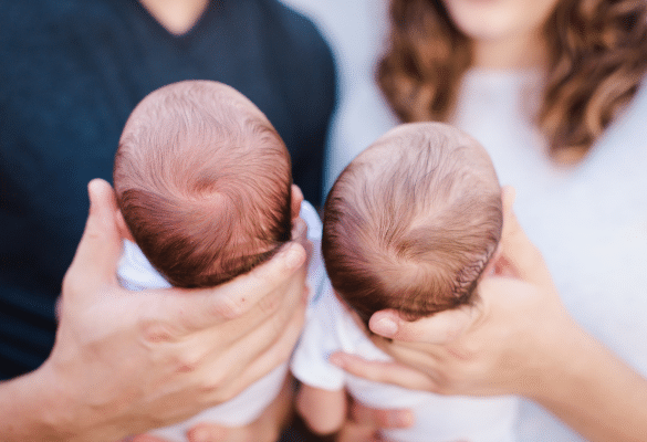 Jeune maman installant deux bébés jumeaux dans leur chambre à la maison, entourée de son conjoint, ambiance douce et familiale.