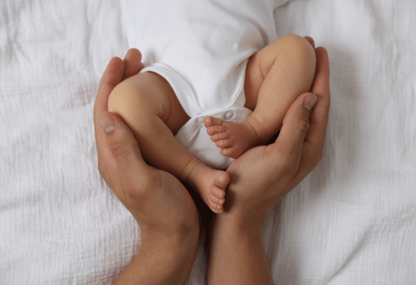 mains d’un parent enveloppant le corps d’un bébé en massage