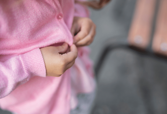 Gros plan sur les mains d'un enfant qui ferme les boutons de son gilet tout seul.