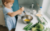 Jeune enfant préparant une recette en mélangeant des ingrédients dans une cuisine adaptée à sa taille.