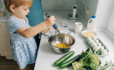 Jeune enfant préparant une recette en mélangeant des ingrédients dans une cuisine adaptée à sa taille.