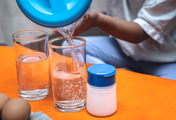 Enfant réalisant une activité de transvasement d'eau avec des verres et un récipient.